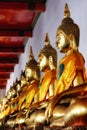 row of golden Buddha statues in a temple. The statues are seated in a row on a red platform. The statues are all identical, with Royalty Free Stock Photo