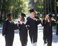 Row of happy young people in graduation gowns outdoors. Students are walking in the park. Royalty Free Stock Photo