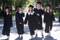 Row of happy young people in graduation gowns outdoors. Students are walking in the park. Royalty Free Stock Photo