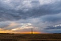 A row of high voltage electrical power lines cling to the horizon in an otherwise vast, wide open rural landscape on sunset with