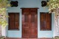 Row house facade background show dark wooden entrance door and windows with steel rod on light blue wall with bamboo plant pot