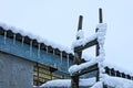 A row of icicles on a slate roof and a wooden ladder under the snow