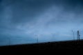 Row of lampposts on the street and a telecommunication tower at the dam with stone wall on a stormy day with unclear sky.