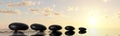 Row or line of black pebbles with water on sunset or sunrise background, zen, spa, yoga or meditation concept Royalty Free Stock Photo