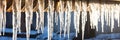 a row of long icicles hanging from the roof of a house on a sunny day panorama Royalty Free Stock Photo