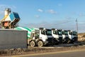 Row of many modern big mixer trucks parked against mobile temporary concrete plant factory at new asphalt road Royalty Free Stock Photo