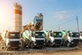 Row of many modern big mixer trucks parked against mobile temporary concrete plant factory at new asphalt road Royalty Free Stock Photo