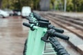 Row of green mint rental motorized kick scooters in the center of rainy city. Electric Urban transportation concept.