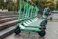 Row of green mint rental motorized kick scooters in the center of rainy city. Electric Urban transportation for every