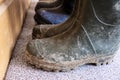 Row of muddy dirty rubber boots in front of a wooden wall