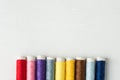 Row of multicolored rainbow palette sewing threads on cardboard spools. White wood background. Crafts hobbies artisan business