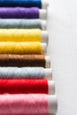 Row of multicolored sewing threads on cardboard spools. White wood background. Crafts hobbies local artisan business Royalty Free Stock Photo