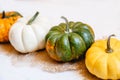 A row of multicolored small pumpkins on burlap on a white wooden background. The focus is one yellow green pumpkin