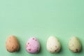 Row of multicolored speckled chocolate eggs on light green turquoise background with linen paper texture. Easter greeting card Royalty Free Stock Photo