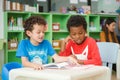 Row of multiethnic elementary students reading book in classroom.