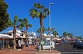 A row of neat commercial retail shops in white with car park at Puerto del Carmen with palm trees & road, Lanzarote island, Spain