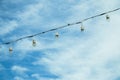 Row of old rustic light bulb hanging on string wired electric with blue sky in the background.