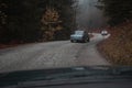 Row of old vintage cars riding on a curvy road in autumn setting. Racing cars from the seventies on a row in a forest