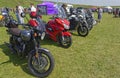 A row of Parked Motorbikes including makes from Triumph, Honda and Harley Davidson on the grass.