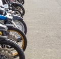 a row of parked motorcycles sit in a parking lot in front of a fence
