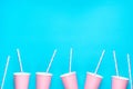 Row of pink empty paper cups striped drinking straws arranged in bottom border on blue background. Creative flat lay. Birthday