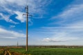 A row of poles of a power line in a field near a dirt road under a clear sky Royalty Free Stock Photo