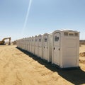 A row of portable toilets is aligned on a sandy construction site under a clear blue sky Royalty Free Stock Photo
