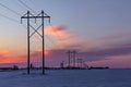 Row of power line poles near a small town at sunset in the Winter Royalty Free Stock Photo