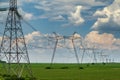 Row of power line support pylons on the green cultivated field with cloudy sky Royalty Free Stock Photo