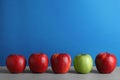 Row of red apples with green one on table against color background. Royalty Free Stock Photo