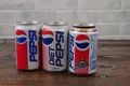 A row of retro aluminium cans of Pepsi against a white brick wall laying on the wooden table