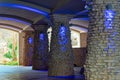 Row of rock and stone pillars holding up rooftop in dark courtyard with blue lanterns on exterior walls in shadow