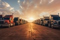 A row of semi trucks parked in a parking lot on sunset. Many trucks in panoramic image