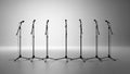 Row of seven black microphone stands silhouetted against a bright white and grey gradient background Royalty Free Stock Photo
