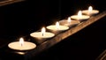 A row of small bright lit votive candles in a dark room, sanctuary, church, cathedral, burning flames. Light in the darkness, hope Royalty Free Stock Photo