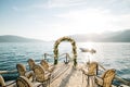 Row of soft chairs in front of a wedding arch on a cobbled pier with the sea and mountains in the background Royalty Free Stock Photo
