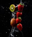 A Row of strawberries and kiwi being doused with plenty of water against a black background Royalty Free Stock Photo