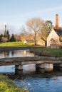 Row of sunny quintessential Cotswold cottages by a river in Cotswolds, England, vertical shot