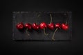 Row of sweet juicy cherries on black stone plate. dark background.