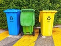 Row of three brightly colored outdoor waste bins lined up on a sidewalk.