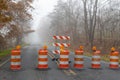 Row of tightly spaced orange traffic barrels barricading a road disappearing into a foggy autumn landscape