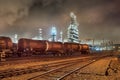 Row of train wagons with an illuminated oil refinery at night in Port of Antwerp, Belgium