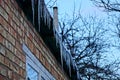 Transparent icicles on the roof of a house against a brick wall background Royalty Free Stock Photo