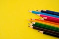 A row of unevenly arranged colored pencils on a yellow background with copy space