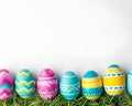 Row of vibrant Easter eggs lined up on green grass against a clean white backdrop, AI-generated. Royalty Free Stock Photo