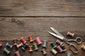 Row of vintage wooden spools of multicolored threads, tailoring scissors, sewing items on wooden board.