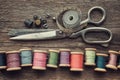 Row of wooden spools of multicolored threads, tailoring scissors, thimbles, measuring tape, sewing items on wooden board.