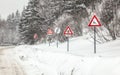 Row of warning roadsign on dangerous part of forest road, during winter blizzard. Caution - deers, snow, skids and Royalty Free Stock Photo