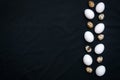 A row of white chicken and quail eggs on a black textile textured uneven background with copy space. Easter concept.