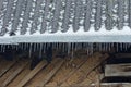 A row of white ice icicles on a gray slate roof covered in snow